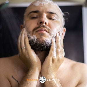 A man with closed eyes, enjoying the sensation of washing his beard with conditioner, featured on the article 