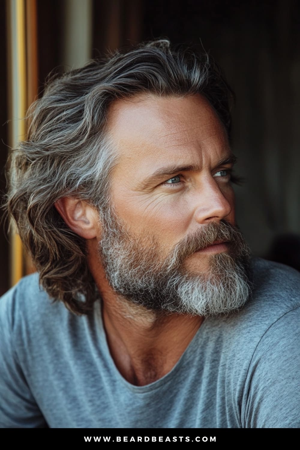 A distinguished older man with a full, well-groomed beard, showcasing long, wavy hair, an excellent example of long hairstyles for older men. His hair flows naturally, with soft waves that add texture and depth, creating a rugged yet refined appearance. The combination of his wavy hair and beard enhances his mature features, giving him a look that is both timeless and effortlessly stylish. This image captures the essence of a relaxed, confident style that perfectly suits men who want to embrace their length with sophistication.