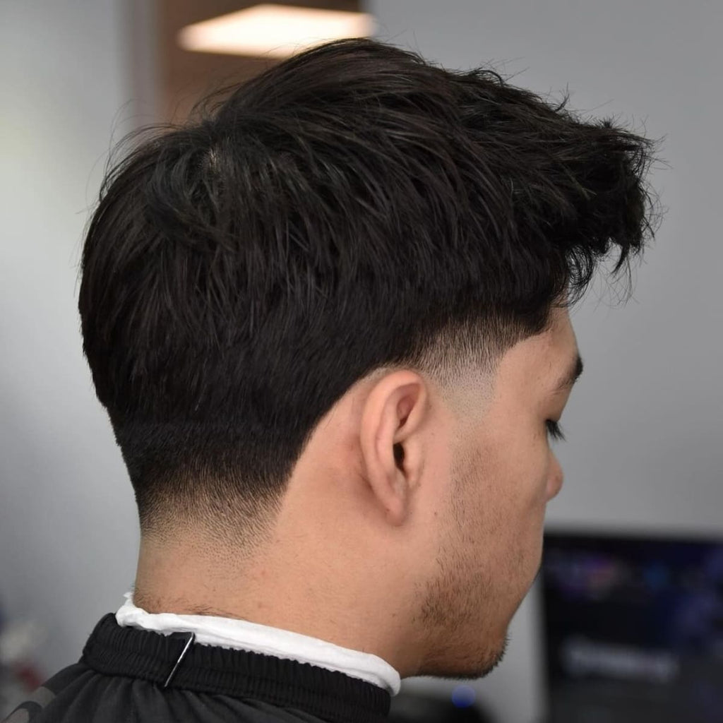 Side view of a man with a low taper fade, showcasing a subtle blend starting just above the ear and gently fading down to the nape. The haircut maintains volume on top with a textured, natural look, creating a soft contrast between the longer hair and the cleanly faded sides. This style offers a refined yet relaxed appearance, perfect for those who prefer a low-maintenance but stylish look.