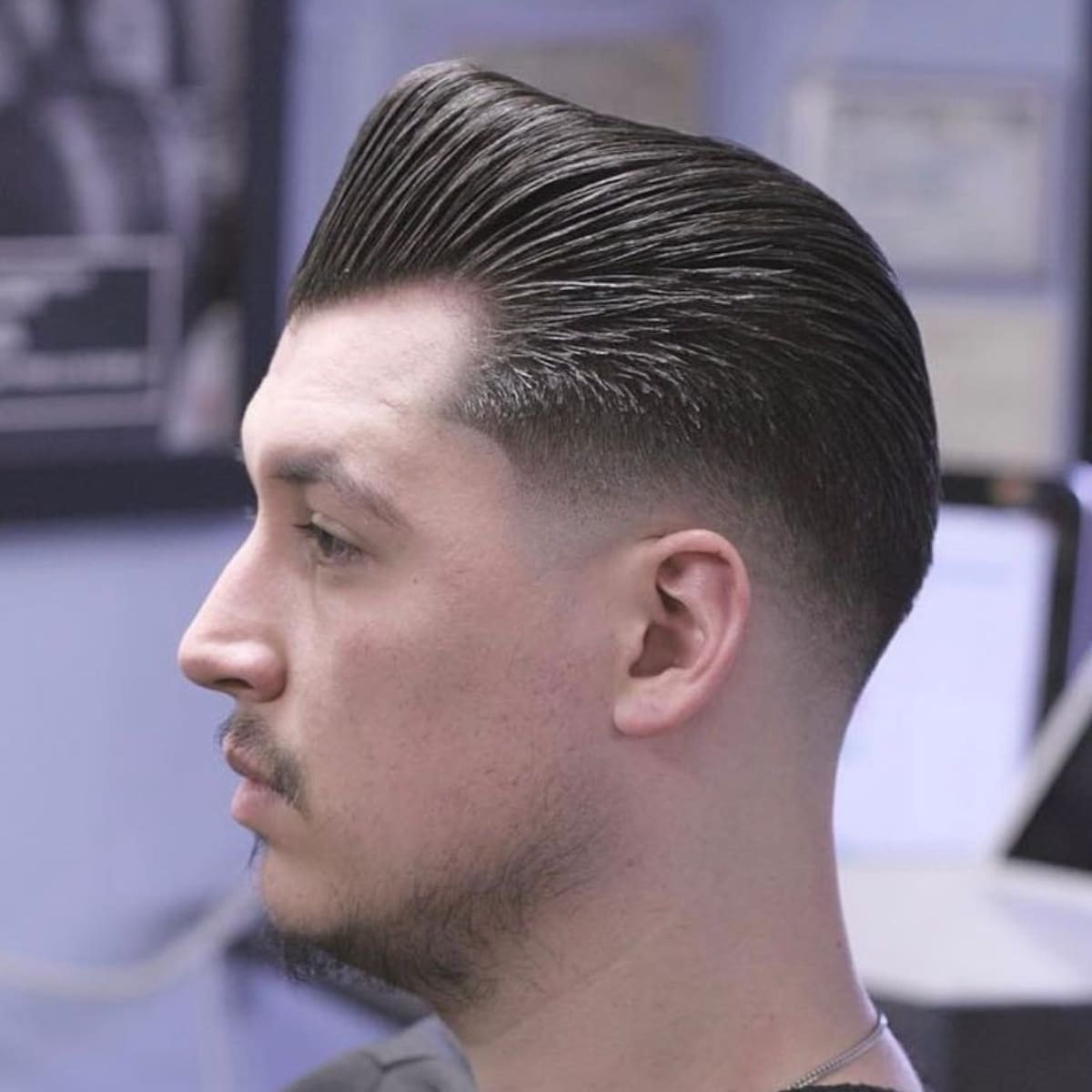 Profile of a man with a sleek, voluminous hairstyle featuring neatly faded sides, captured in a classic barbershop setting.