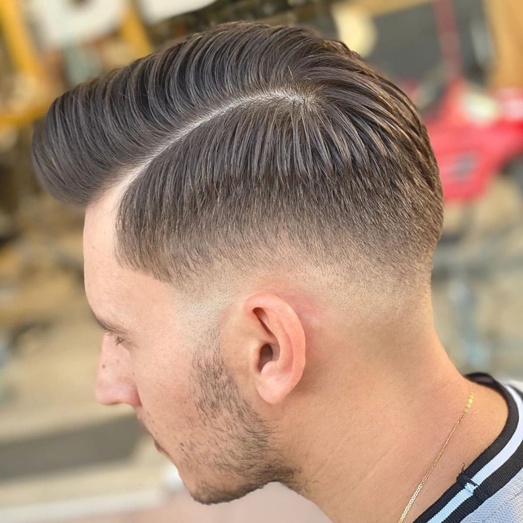 A side profile of a man with a classic side-part hairstyle featuring a clean fade. The hair is neatly parted, with a well-defined line separating the longer top from the closely cropped sides, creating a polished and structured appearance. The fade is gradual, blending seamlessly from the top to the skin near the ear, adding a modern touch to this timeless style. This haircut provides a balanced look that enhances facial structure and adds a sense of refinement.