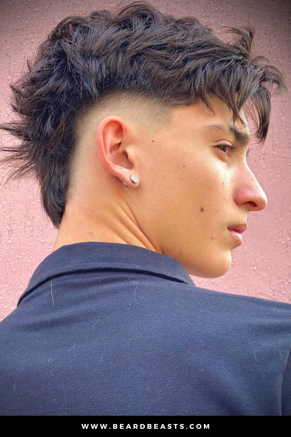 Side profile of a young man with a Modern Mohawk, featuring a textured, tousled top that tapers into a clean, shaved design on the sides. The hairstyle blends edgy elements with a contemporary flair, creating a bold yet stylish look.