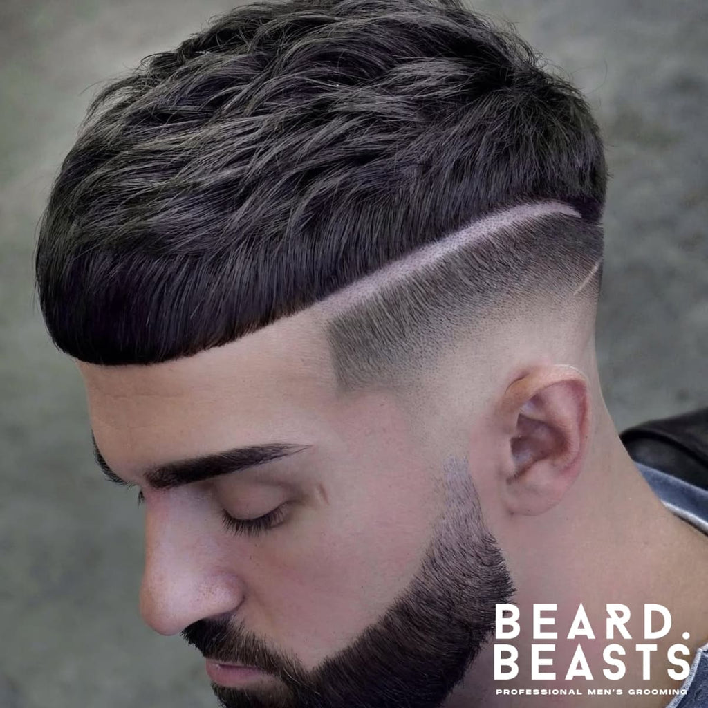 Close-up portrait of a man featuring a sharp, modern haircut with a defined hard part separating the textured top from the cleanly tapered fade on the sides. The hairstyle showcases precision barbering, complemented by neatly groomed eyebrows and a full, styled beard. The man’s thoughtful expression and soft lighting emphasize the details of the haircut and beard. A striking example of a polished and structured men’s hairstyle.