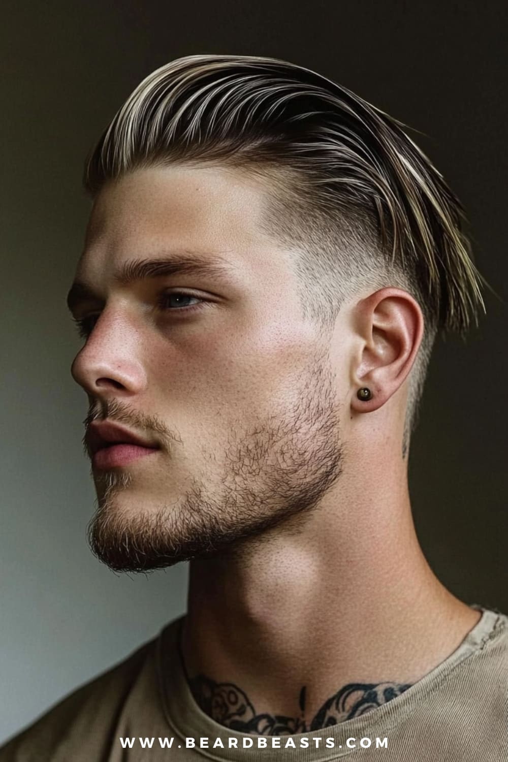 A man showcases a sleek undercut, a popular choice among guys with straight hair. His straight hair is styled back smoothly, creating a polished look with a slight sheen. The sides are sharply faded, emphasizing the contrast between the longer top and the close-cropped sides. He has a well-groomed beard and is accessorized with a small earring and visible neck tattoos, adding an edgy touch to his overall appearance.
